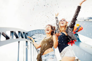 Two young women throwing confetti into the air and looking up, Two young women throwing confetti into the air and looking up,